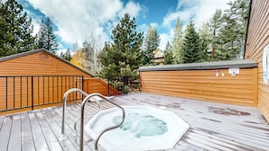 A wooden deck with a hot tub, metal railings, and a wooden cabin in a forested area.