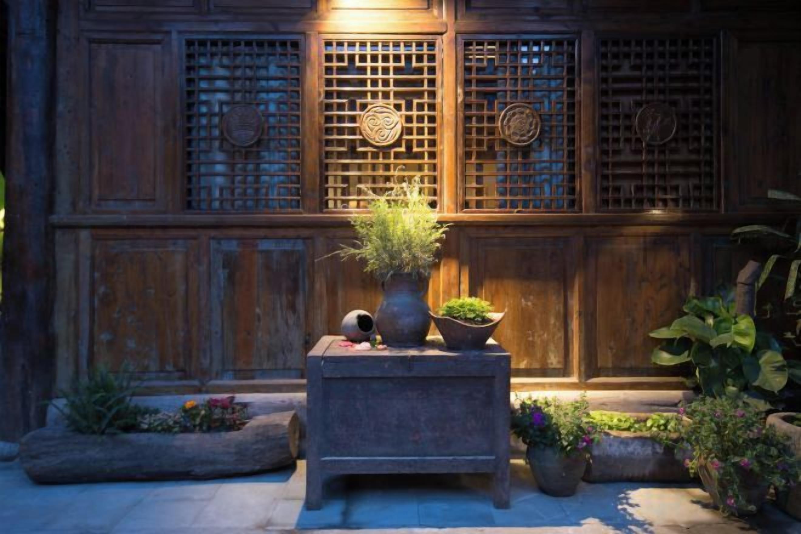 A courtyard with a wooden wall, potted plants, and a stone bench.