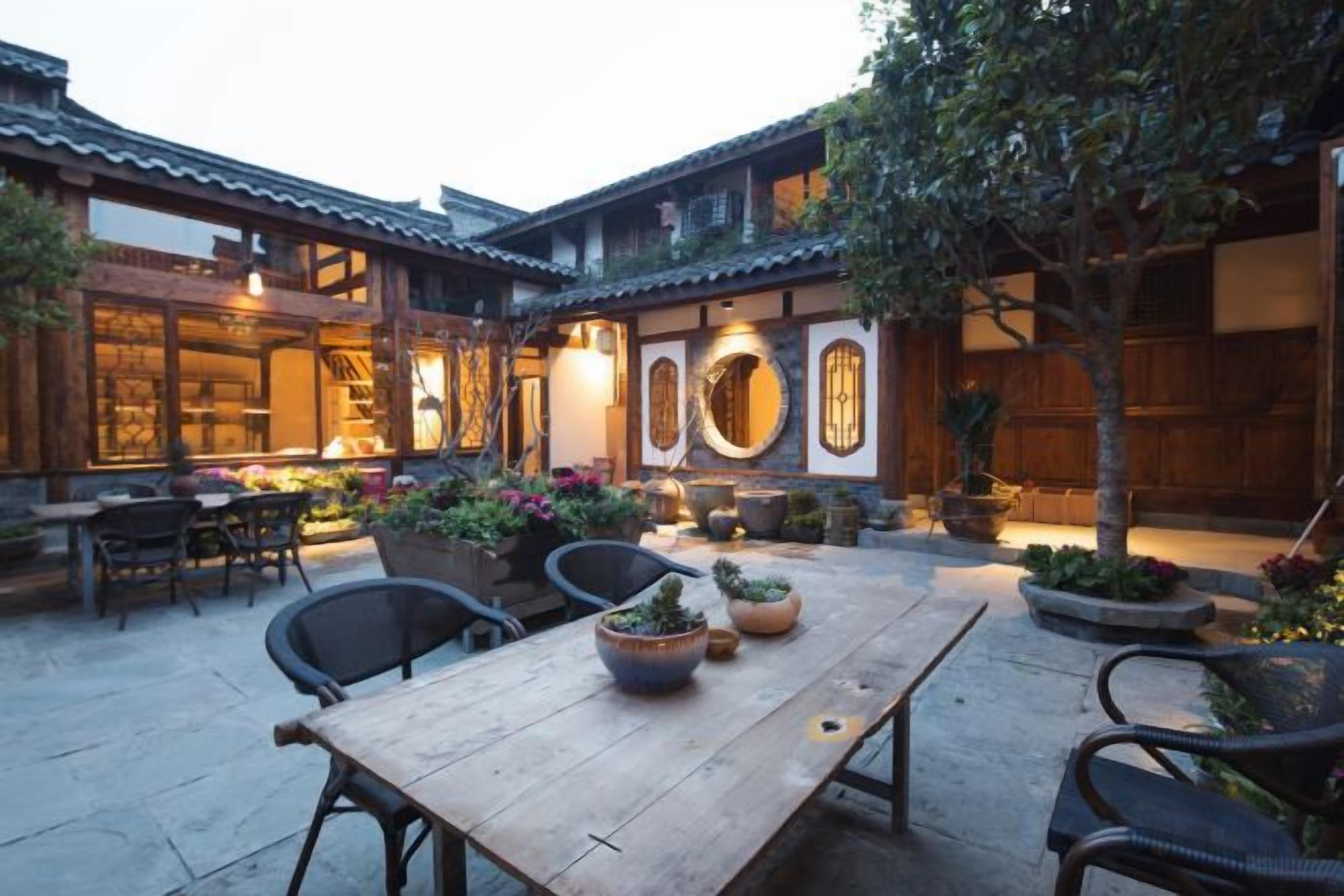 A courtyard with a wooden table, chairs, and potted plants.