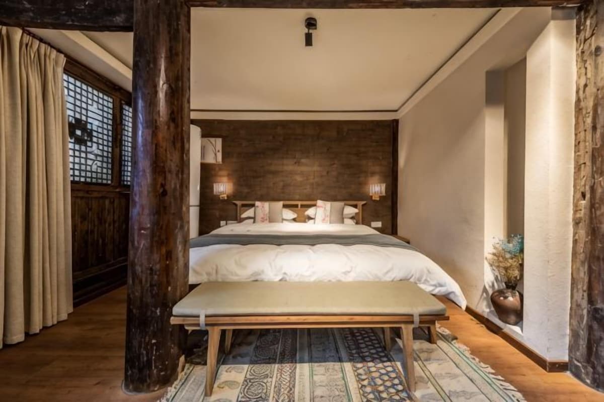 Une chambre avec un grand lit, des poutres en bois, un banc et un tapis à motifs.