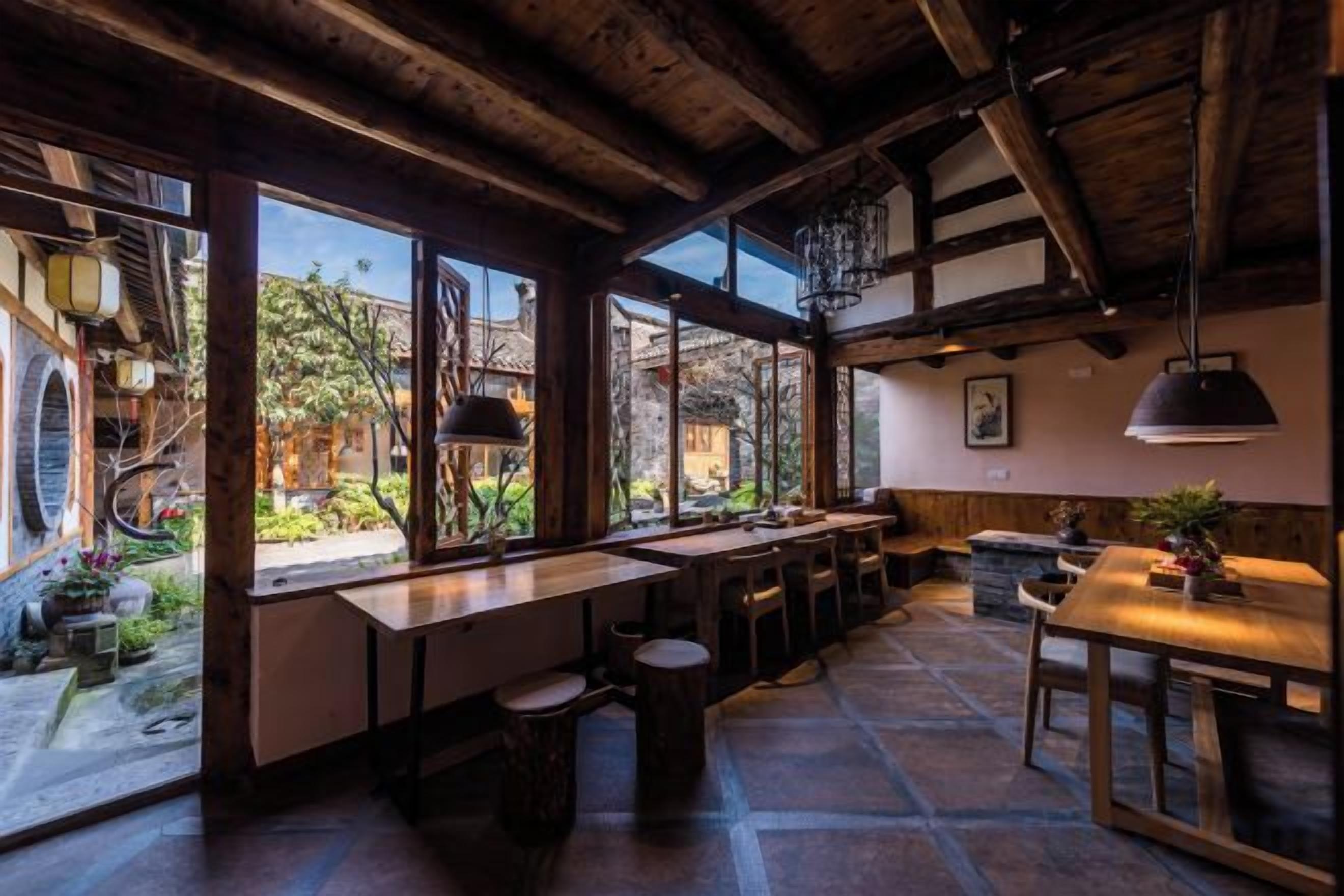 A rustic interior with exposed wooden beams, large windows, and a stone floor.