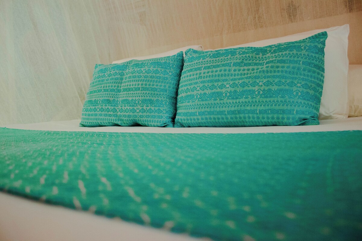 A bed with a green patterned bedspread and two pillows with a similar pattern.