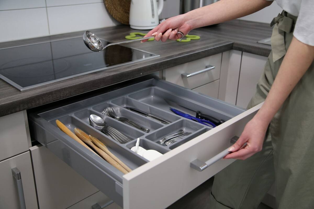 A kitchen drawer with utensils and a person holding a utensil.