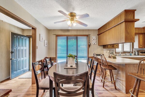 A dining area with a round table, wooden chairs, a ceiling fan, and a kitchen with wooden cabinets and a sink.