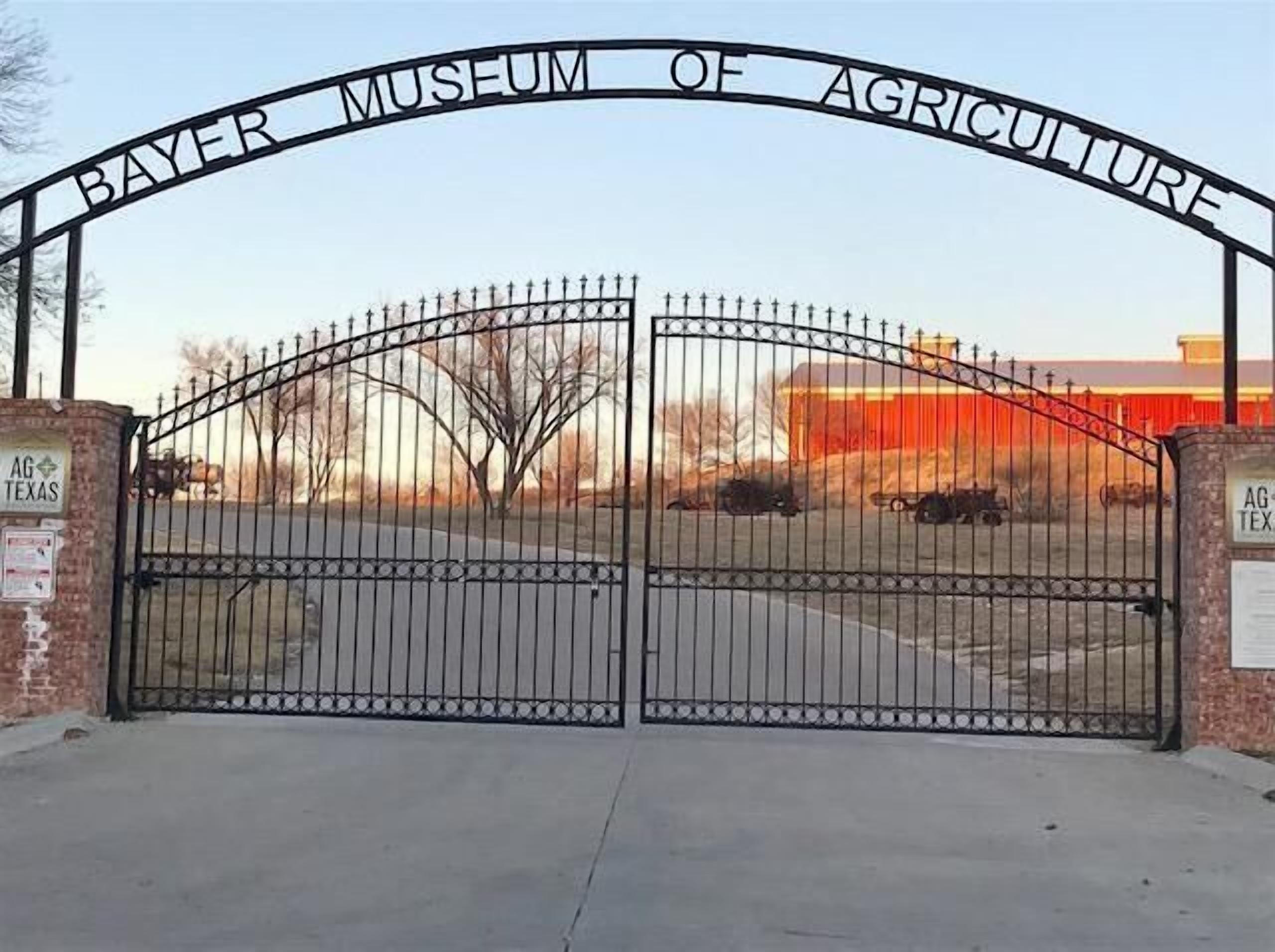 A gated entrance to the Bayer Museum of Agriculture with a clear sky and a building in the background.