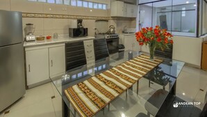 A modern kitchen with a glass dining table, white cabinets, a stove, and a refrigerator. - Apartments Stunning View San Blas (Cusco)
