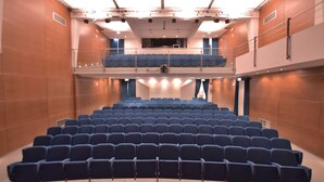 Un teatro con filas de asientos azules, un balcón y una zona de escenario.