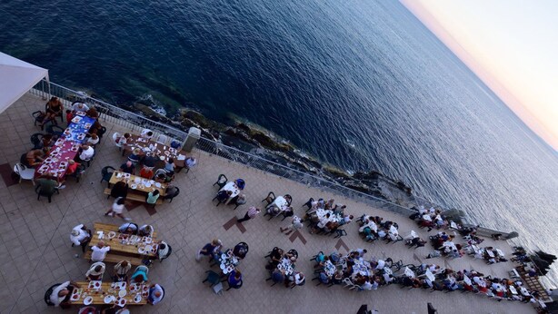 Un área de comedor al aire libre con mesas y sillas dispuestas en una terraza con vistas al mar.