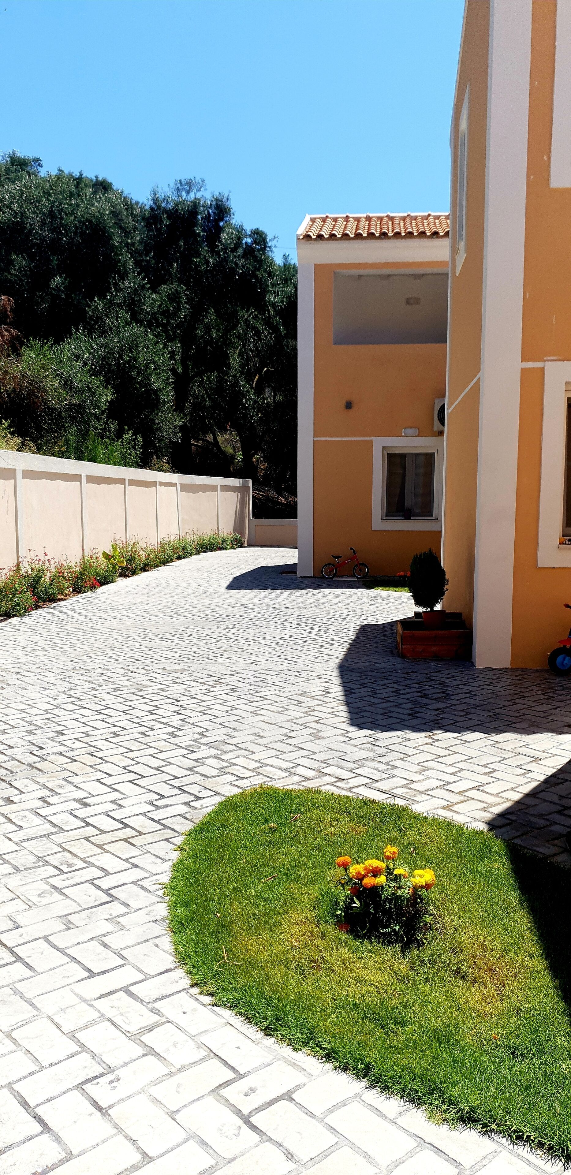 A paved courtyard with a small lawn area, a building with a tiled roof, and a window.
