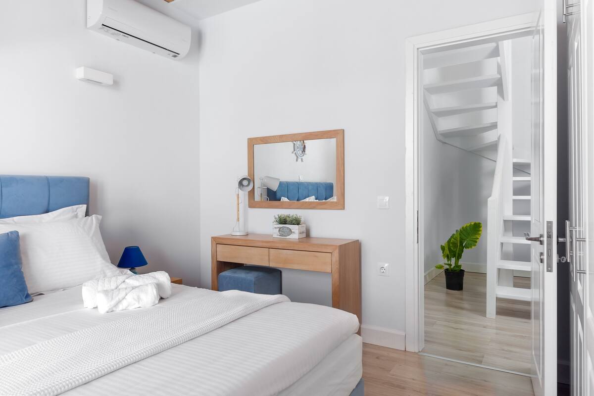 Een slaapkamer met een bed, een houten bureau, een spiegel, een potplant en een trap naar een verdieping boven.