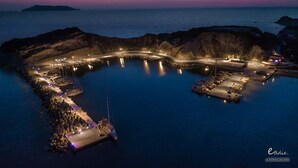 Vue aérienne d’une marina côtière au crépuscule, avec des quais et des bateaux illuminés.