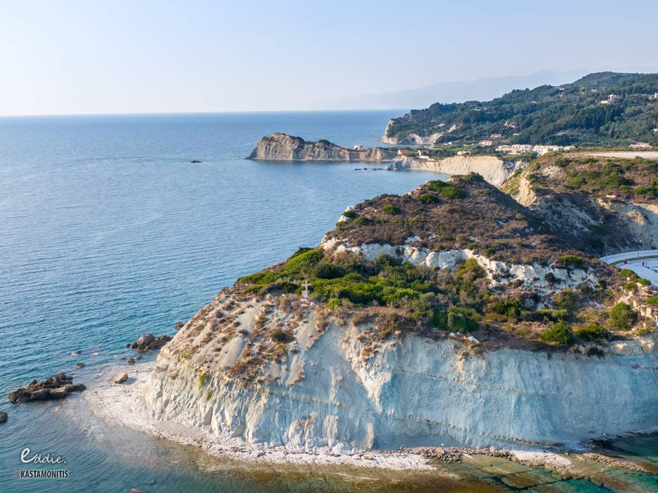 A coastal landscape with cliffs, a clear sea, and distant buildings.
