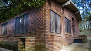 Un bâtiment en briques avec deux fenêtres et une porte, des fondations en béton et un petit auvent.