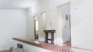 Une pièce aux murs en briques blanches, avec une cheminée et un coin salon comprenant un fauteuil à rayures et un coussin.