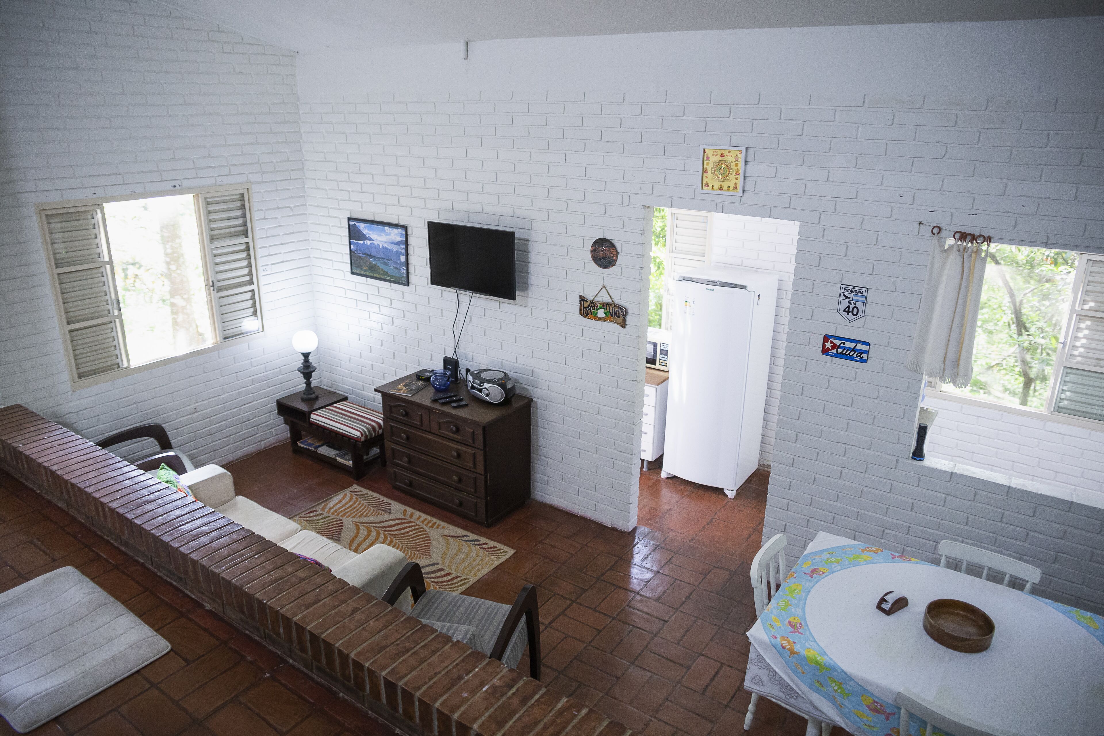 Una habitación con sofá, televisor montado en la pared, un mueble pequeño y una mesa de comedor con un tazón.