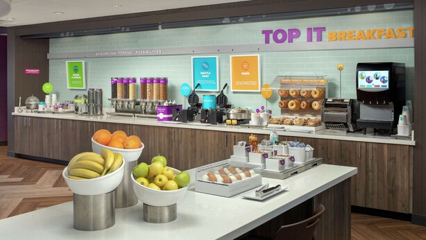 A breakfast area with a counter displaying various food items and a TV screen. - Tru by Hilton Lubbock Southwest (Lubbock)