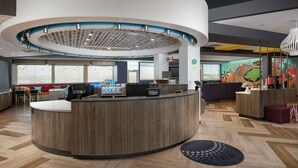 A modern hotel lobby with a curved reception desk, seating area, and large windows offering views of the outside. - Tru by Hilton Lubbock Southwest (Lubbock)