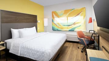 Una camera d'albergo con un letto, una scrivania, una sedia da ufficio, una lampada e un grande quadro astratto appeso al muro.