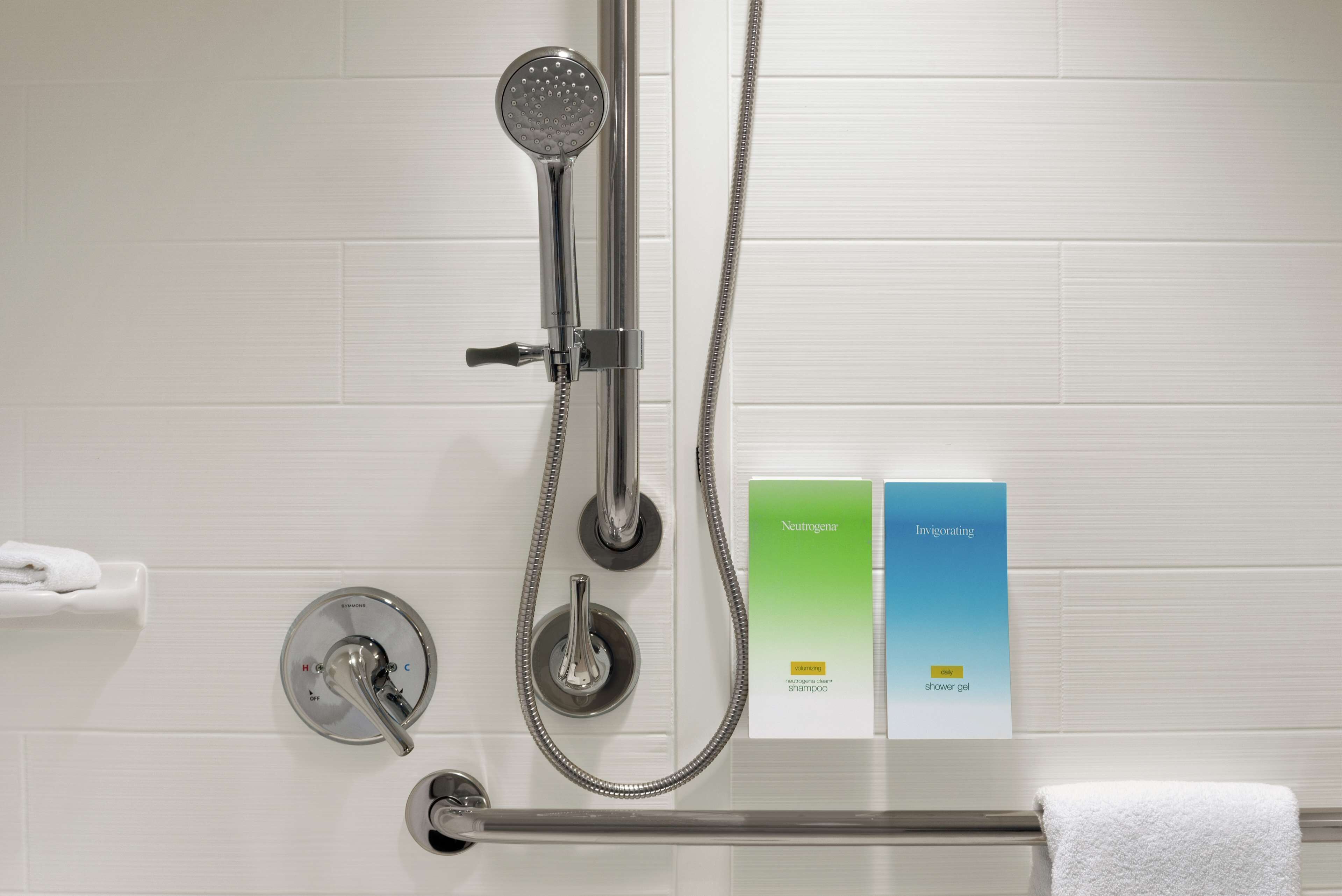Una ducha con cabezal de ducha de mano y un accesorio de ducha manual. Hay dos botellas de gel de ducha en la pared.