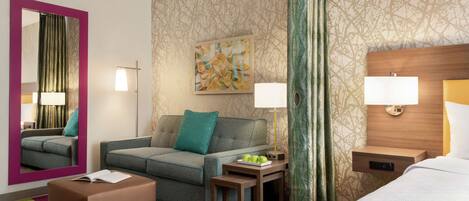 Hotelkamer met een bank, een klein tafeltje met lamp, nachtkastje met lamp, bed, spiegel en een muur met een geometrisch patroon.