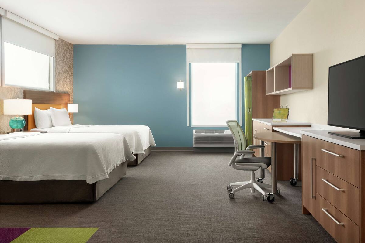 Hotelkamer met twee bedden, een bureau met stoel, een flatscreen televisie en een raam met zonwering.