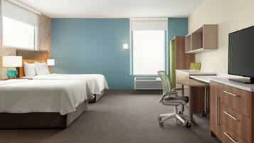 A hotel room with two beds, a desk with a chair, a flat-screen TV, and a window with blinds.