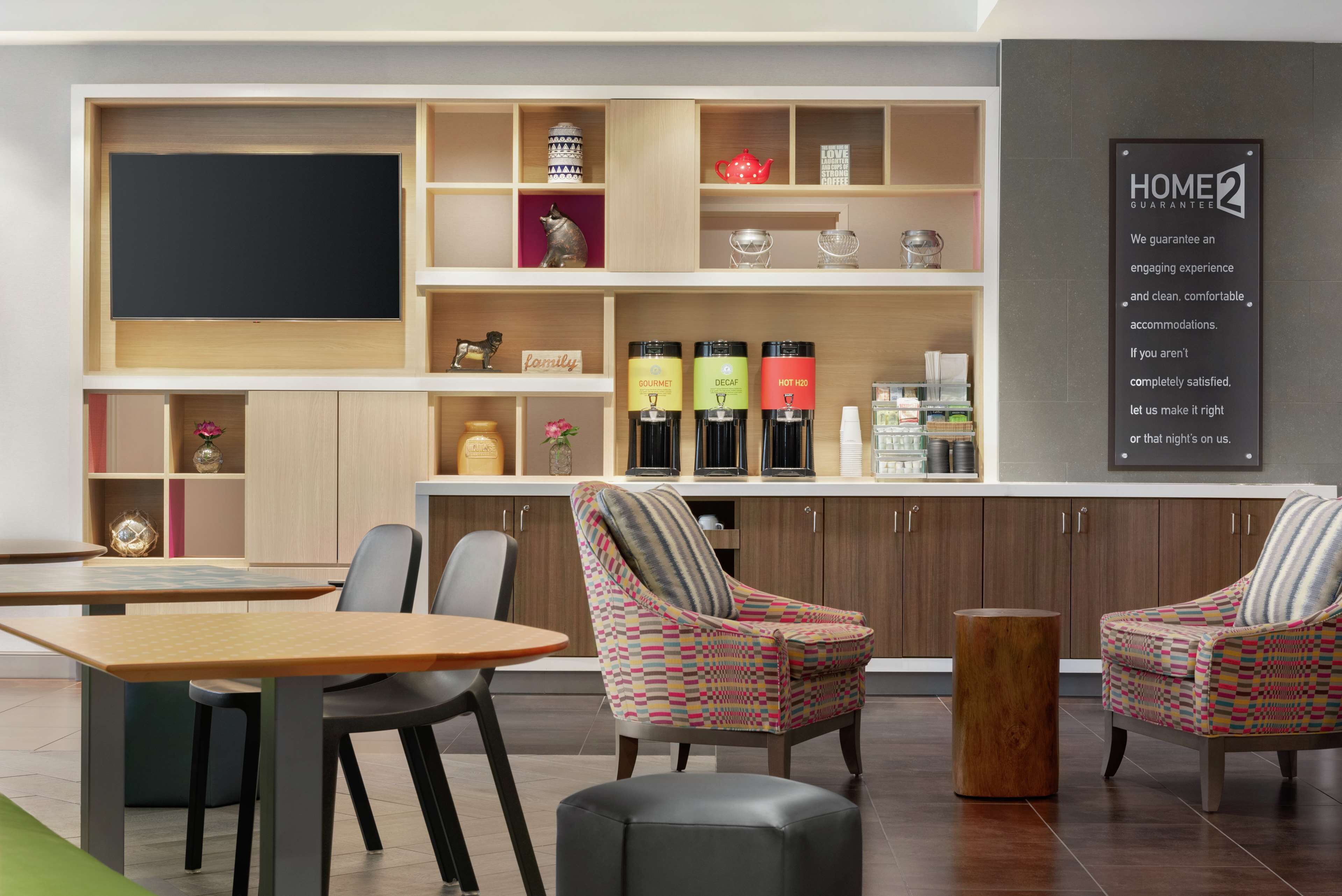 Une chambre d’hôtel moderne comprenant un coin repas, deux fauteuils à motifs, une table basse en bois et un coin cuisine équipé d’une machine à café et d’une bouilloire.