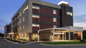 A multi-story hotel with a modern design, featuring a covered outdoor area with seating and a barbecue. - Home2 Suites by Hilton Overland Park (Overland Park)