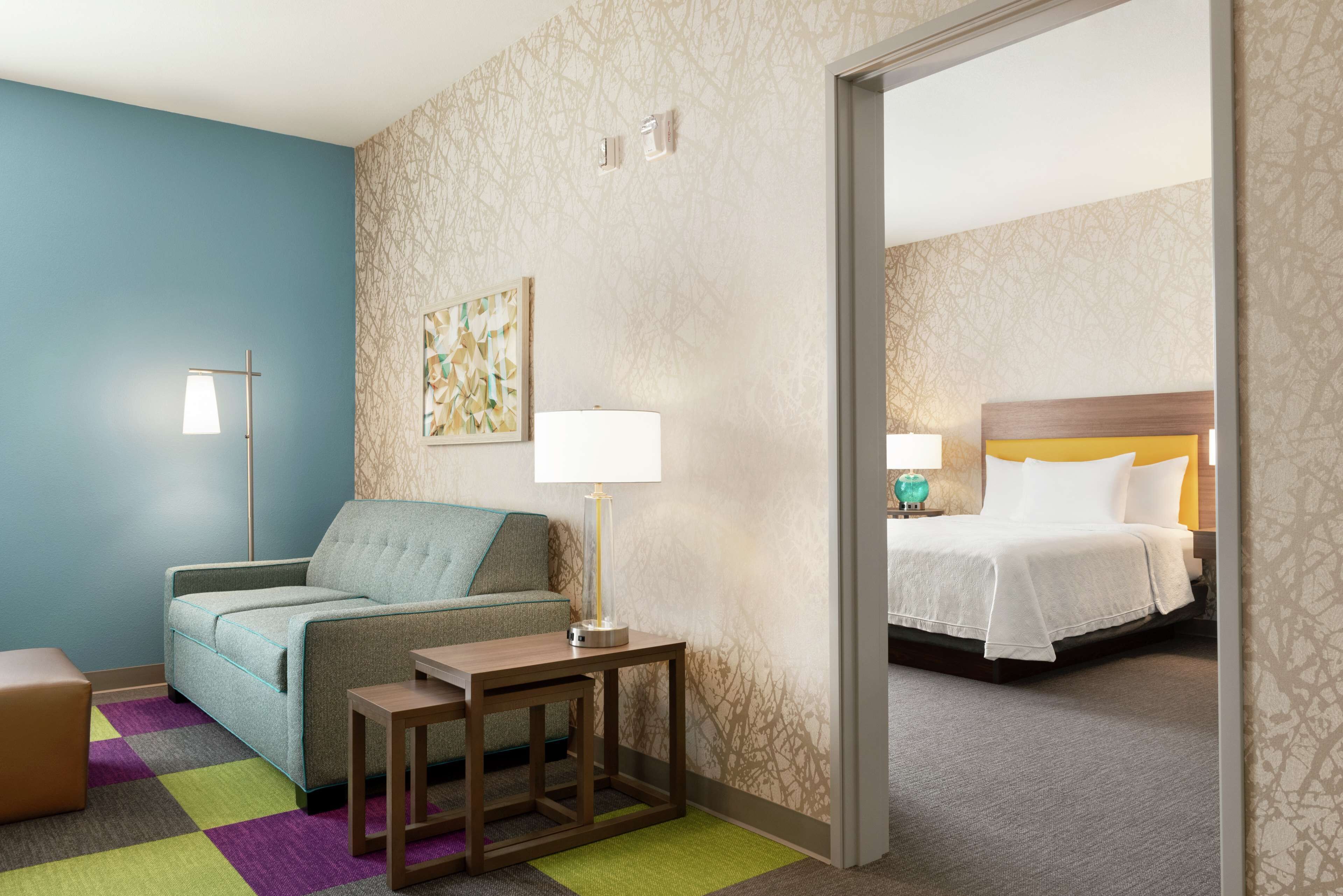 Una habitación de hotel con sofá, una mesita, una lámpara y una cama con cabecera.