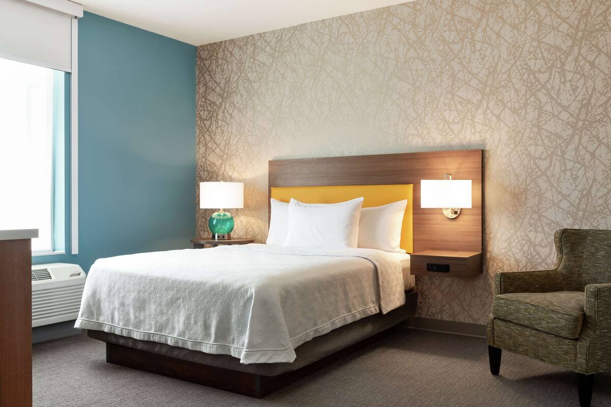 Een hotelkamer met een bed, twee bedlampen, een stoel en een wand met een decoratief patroon.
