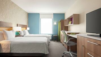Quarto de hotel com duas camas, uma escrivaninha com computador, televisão e janela com persianas.