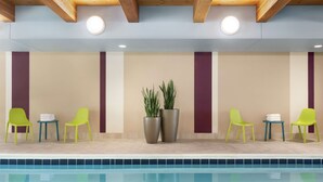 A poolside area with a pool, green chairs, a small table with towels, and potted plants. - Home2 Suites by Hilton Overland Park (Overland Park)