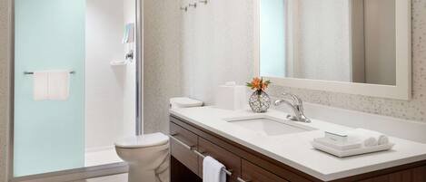 A modern bathroom with a glass shower door, a white toilet, a sink with a vase of flowers, and a large mirror.