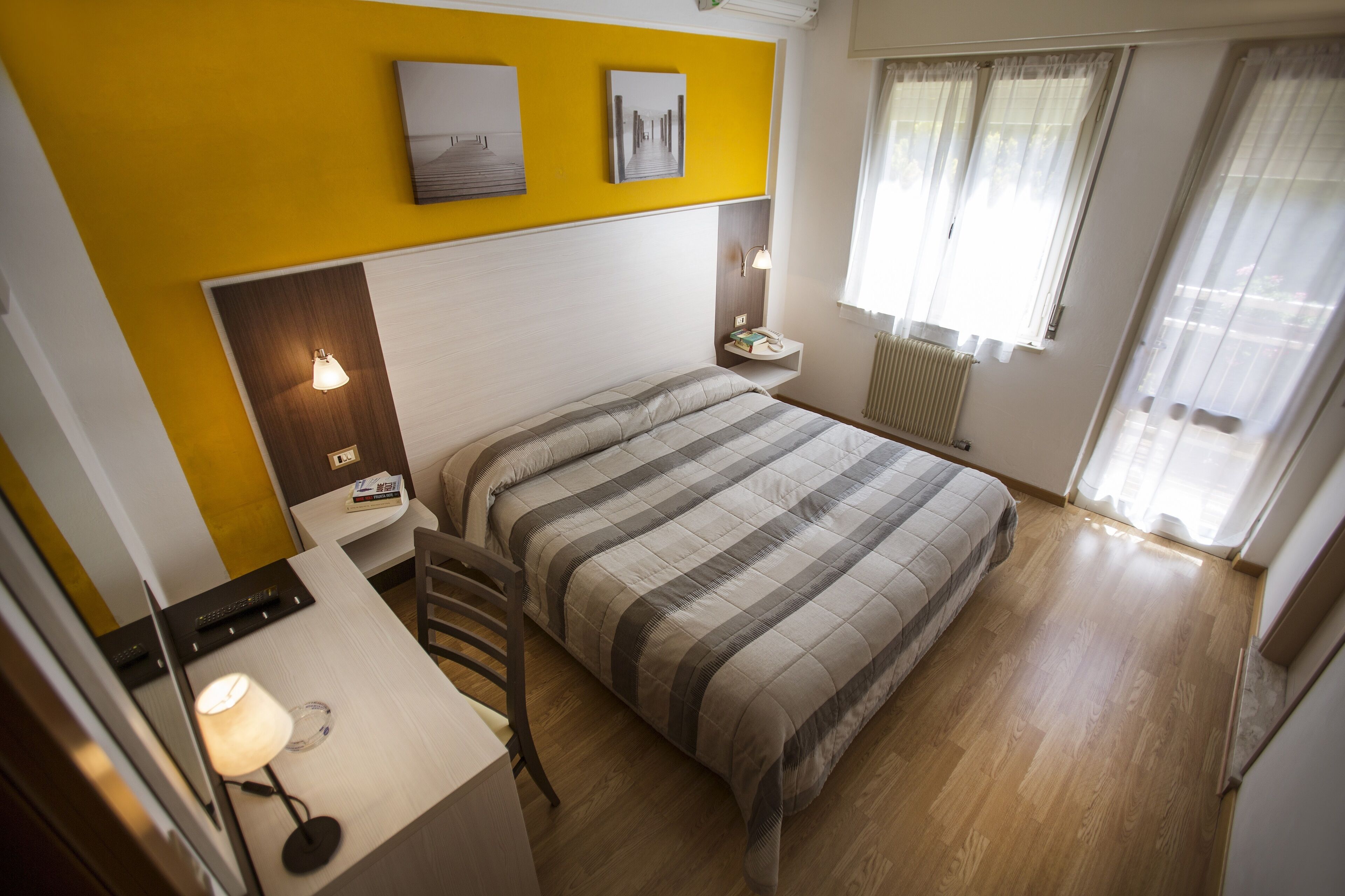 Une chambre d’hôtel avec un lit, une table de chevet, une lampe et une vue sur l’extérieur par une fenêtre.