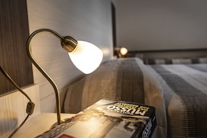 A bedside table with a magazine, a lamp, and a bed with striped bedding.