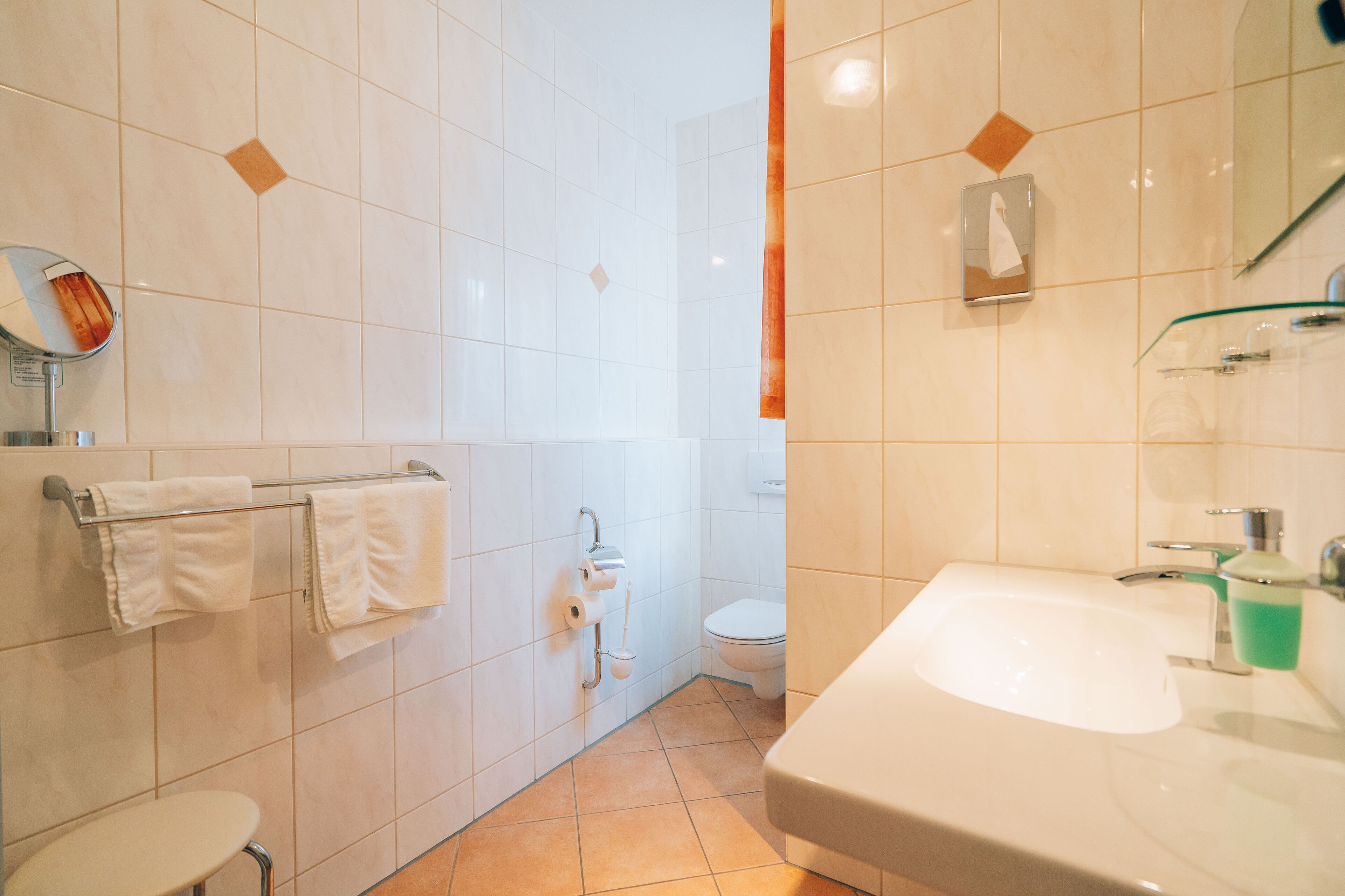 A bathroom with white tiles, a sink, a toilet, and a mirror.