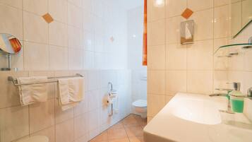 A bathroom with white tiles, a sink, a toilet, and a mirror.