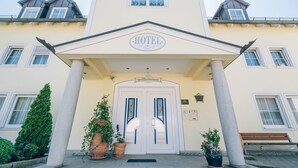 A hotel entrance with a white facade, a central entrance door, and two columns. - Hotel Abenstal (Au in der Hallertau)