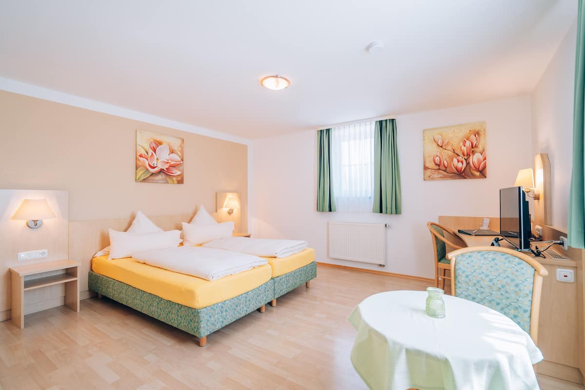 A hotel room with a bed, bedside table, lamp, desk, chair, and a table with a candle.