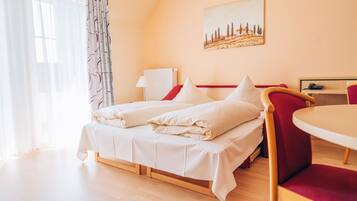 A hotel room with a bed, a chair, a table, and a painting on the wall.