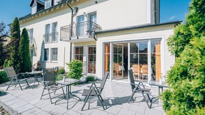 A modern two-story building with a patio area featuring outdoor furniture and a glass door entrance. - Hotel Abenstal (Au in der Hallertau)