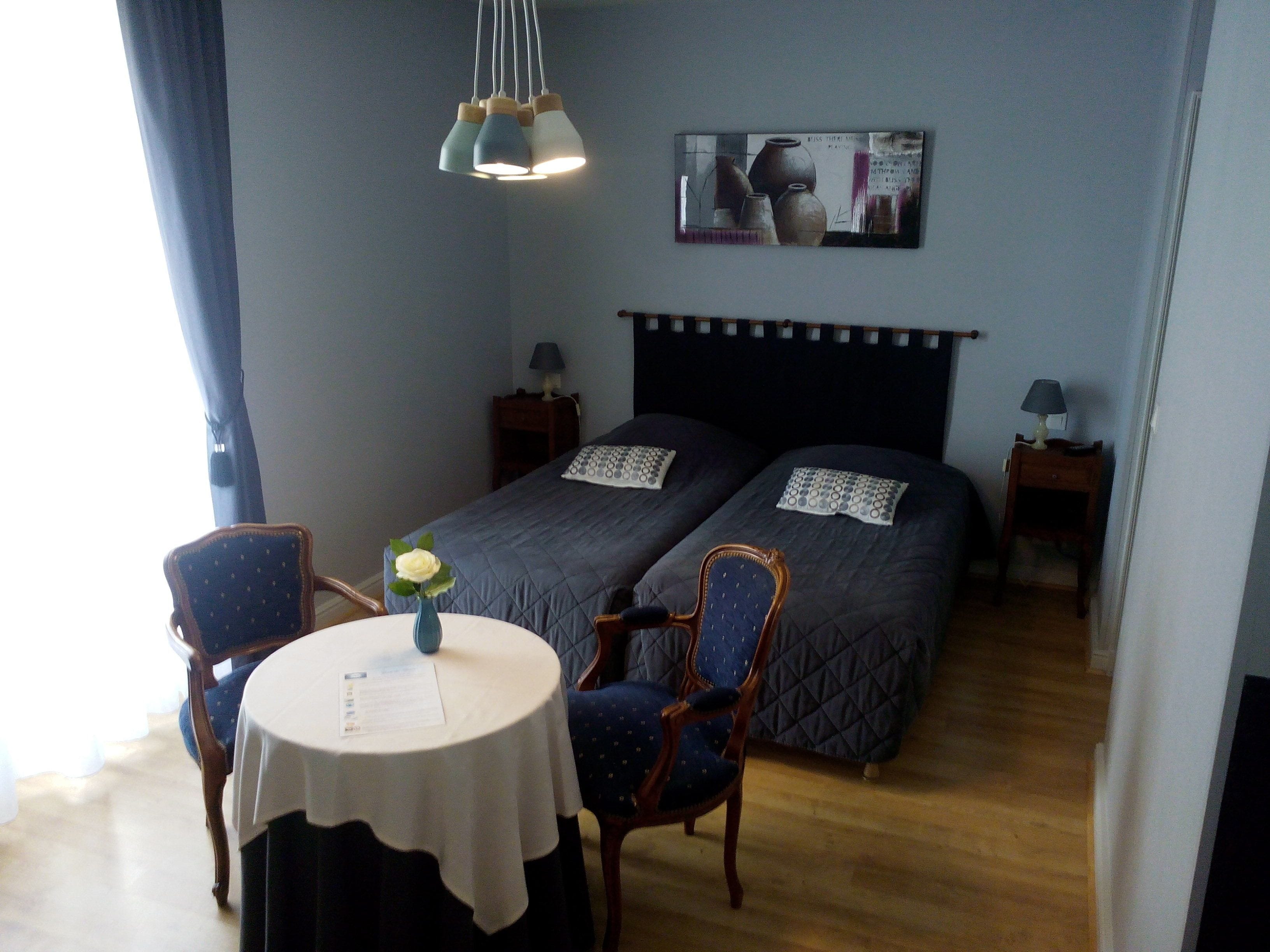 A bedroom with two beds, a table with a vase, and a painting on the wall.