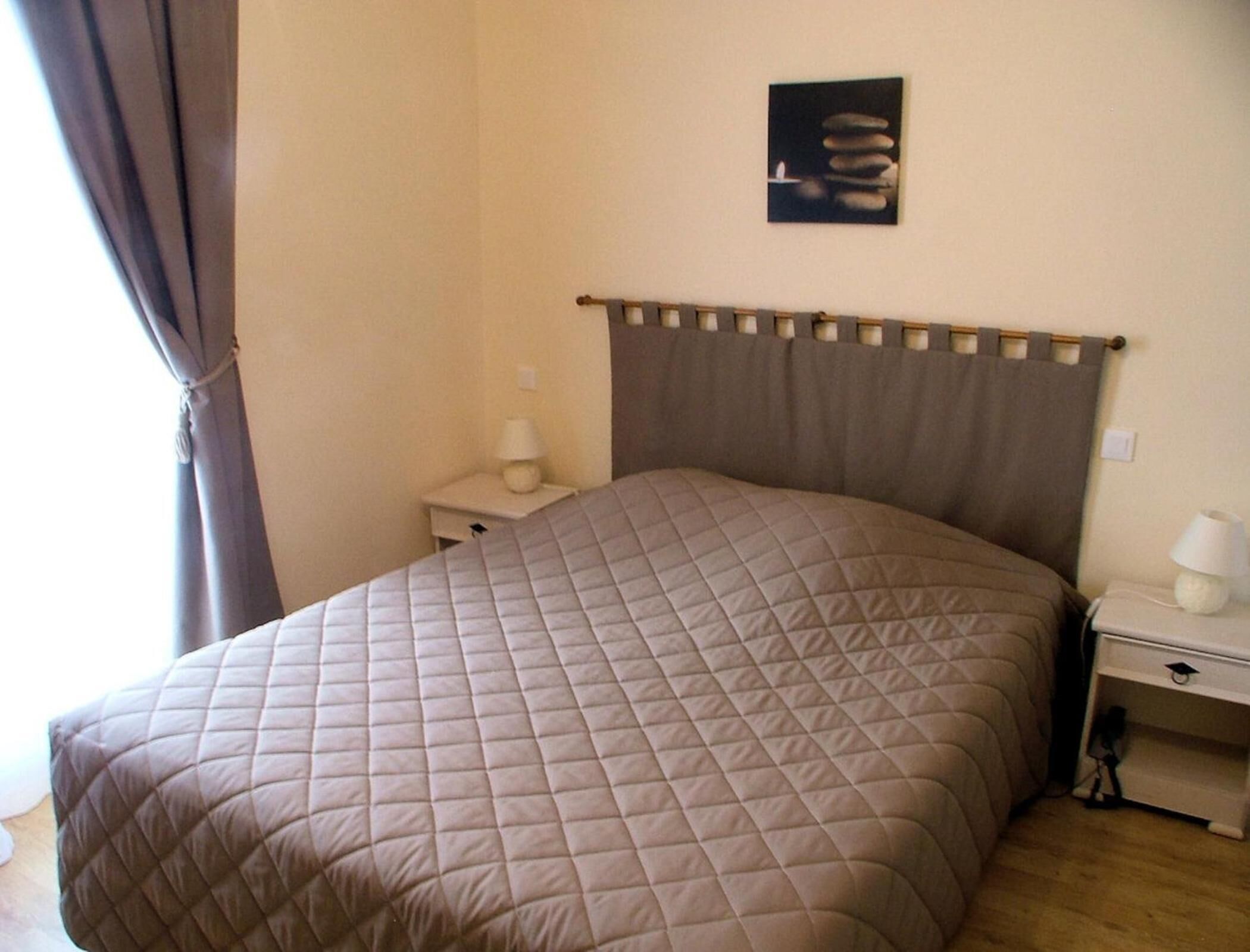 A neatly made bed with a quilted headboard, a bedside table with a lamp, and a wall-mounted artwork.