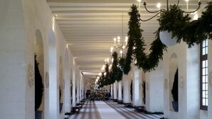 Un largo pasillo con piso a cuadros, paredes blancas y candelabros.