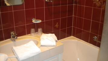 A bathroom with a white bathtub, a sink, and a mirror. There are two towels on the sink and a soap dish on the wall.