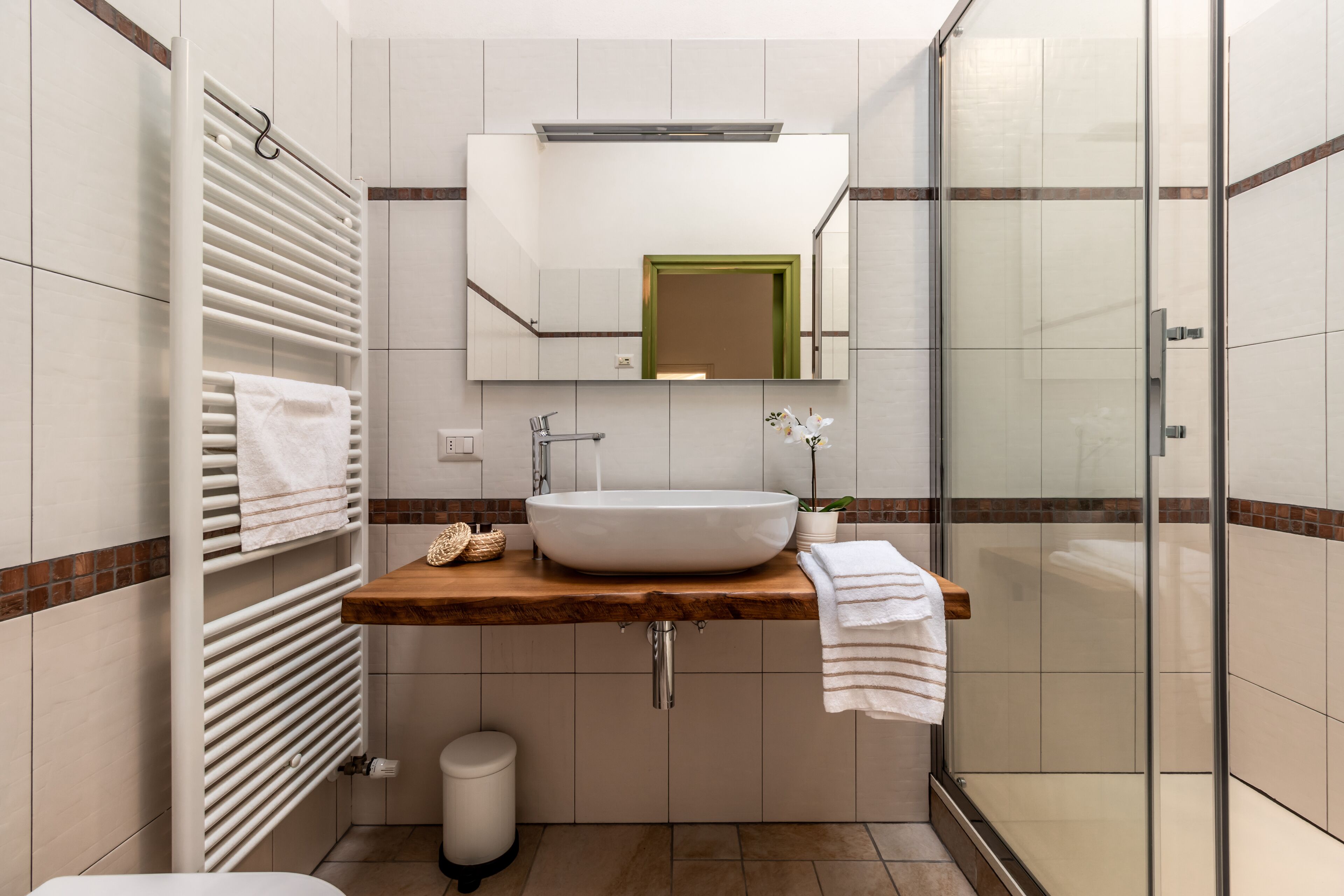 Un bagno moderno con un ampio specchio, un mobile bagno in legno, un lavandino bianco e una cabina doccia in vetro.
