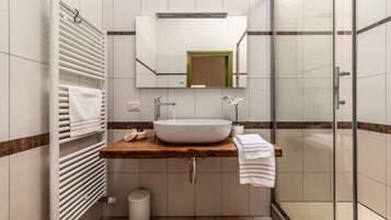 Un bagno moderno con un ampio specchio, un mobile bagno in legno, un lavandino bianco e una cabina doccia in vetro.