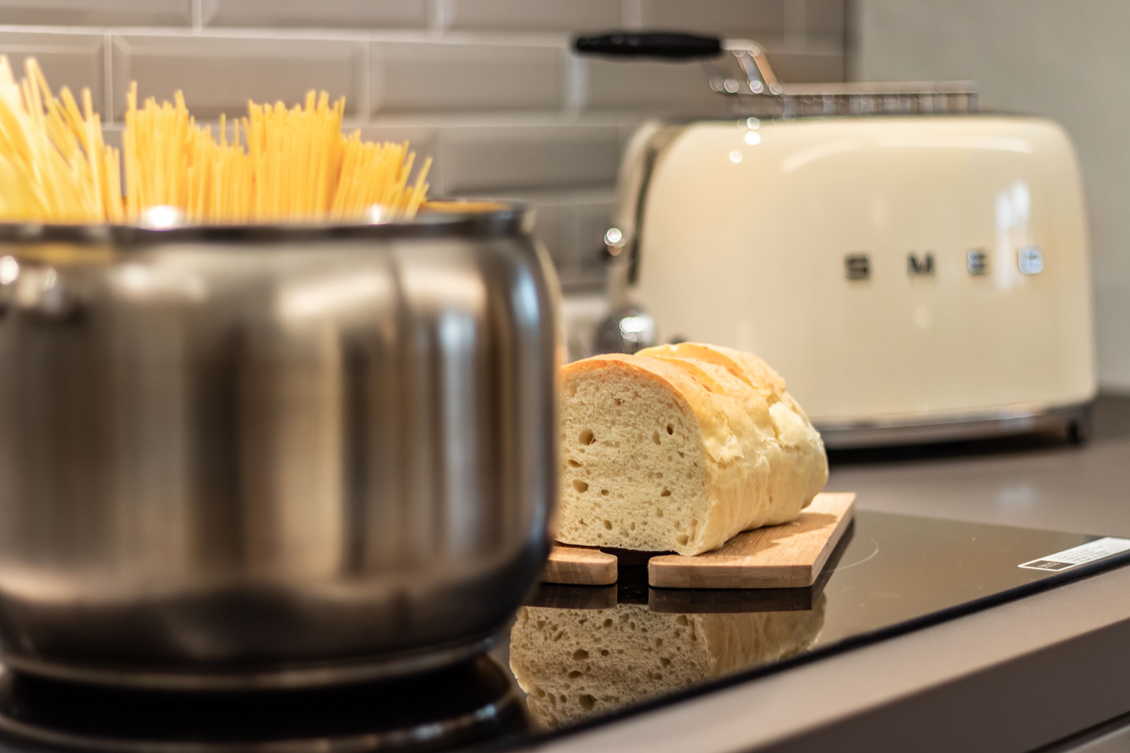 Une cuisine avec une casserole en acier inoxydable, une miche de pain sur une planche à découper en bois et un grille-pain blanc.