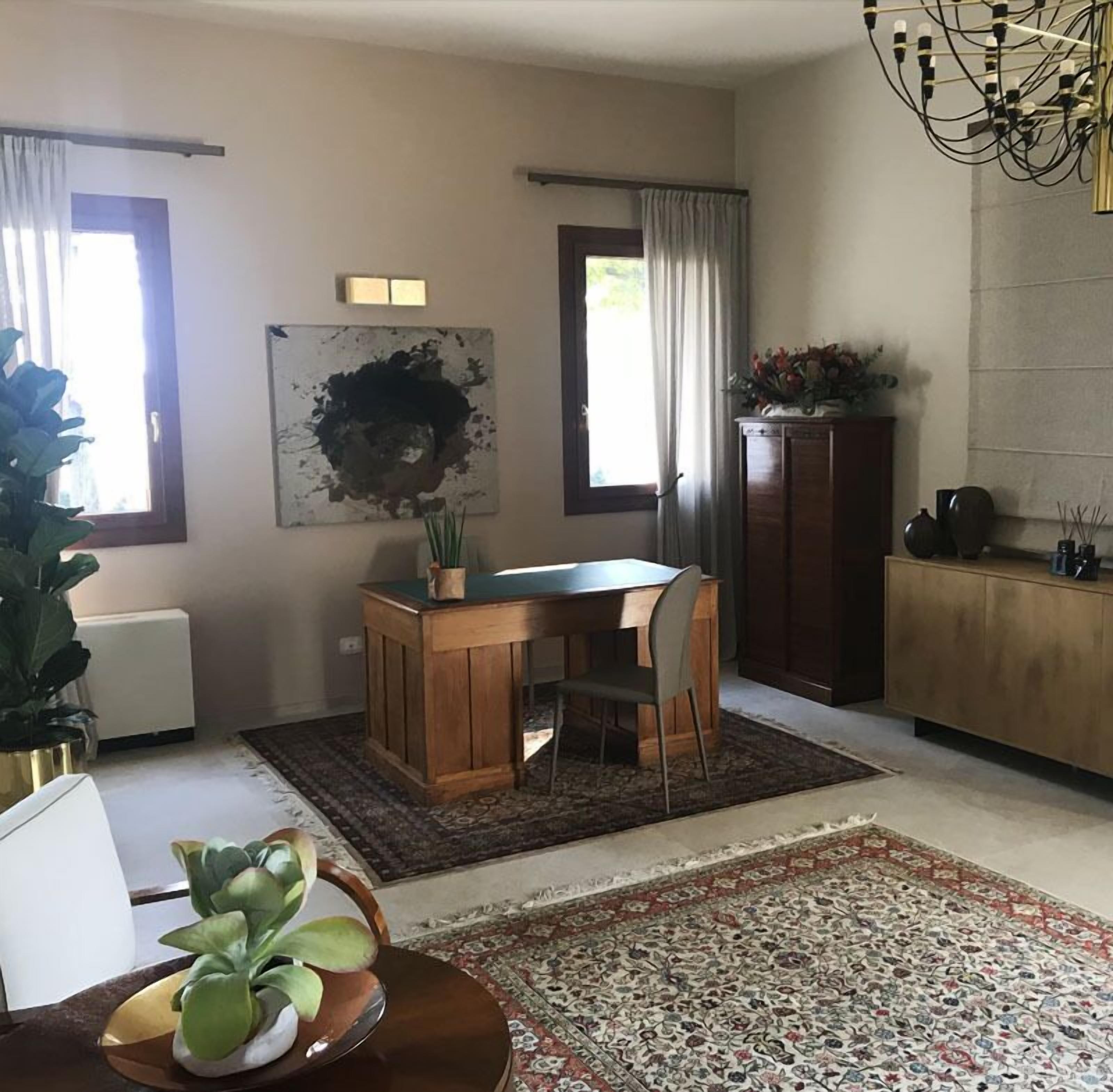 A modern dining area with a wooden table and chairs, a large abstract painting, and a cabinet with decorative items.