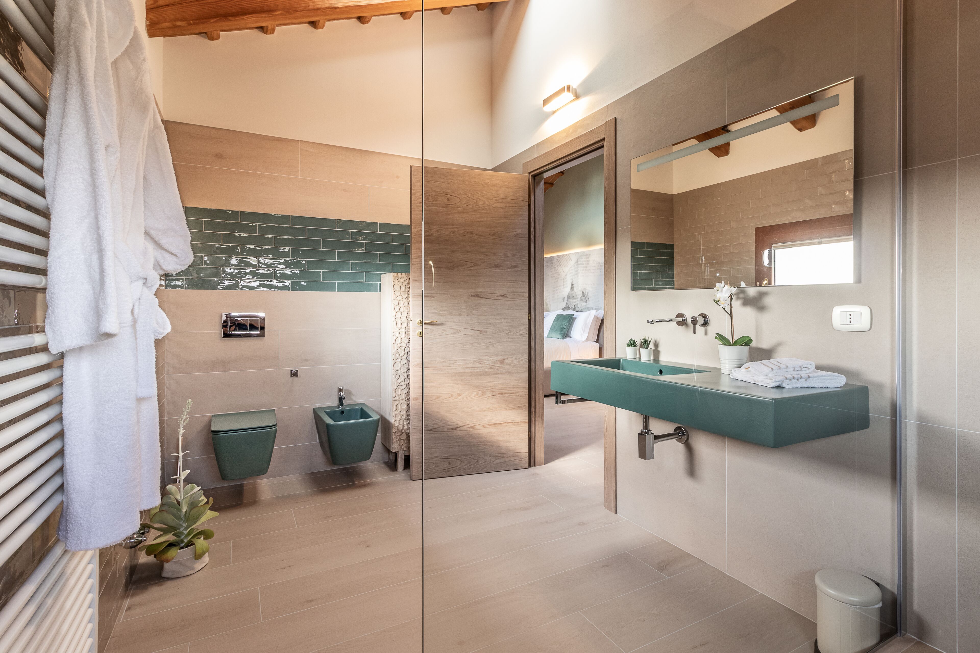 A modern bathroom with a glass shower enclosure, a wooden vanity, and a green tiled backsplash.